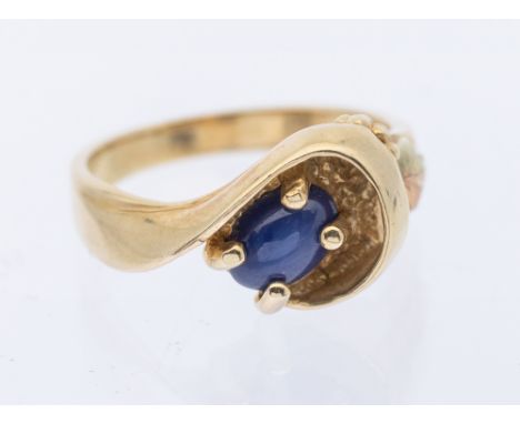 A sapphire and 10k gold ring, comprising an oval cabochon star sapphire measuring approx 5mm, within a scrolled gold sweep, w