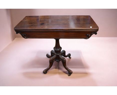 A Victorian mahogany fold over tea/card table with ornate supports standing on four splayed carved legs with castors.