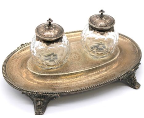 A Victorian silver desk ink stand, of oval shape with ribbed edging, engraved decoration and upon four splayed masked feet, w