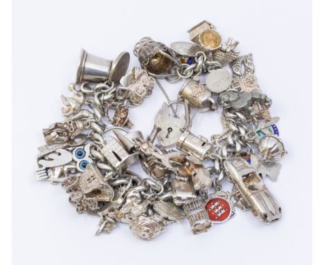 A vintage silver curb link bracelet suspending various silver and white metal charms including enamel versions, along with wa