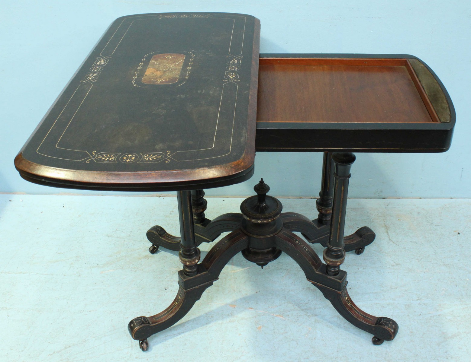 A Victorian ebonised folding card table, the inlaid top lifting to