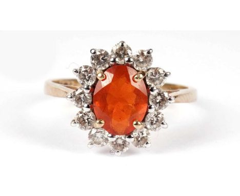 A fire opal and diamond cluster ring, the oval facet-cut fire opal 7.9 x 6.0 x 3.7mm, surrounded by twelve brilliant cut diam