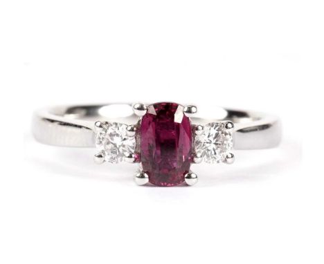 A three stone ruby and diamond ring, the central oval facet-cut ruby, flanked by a pair of brilliant-cut diamonds, on a plati