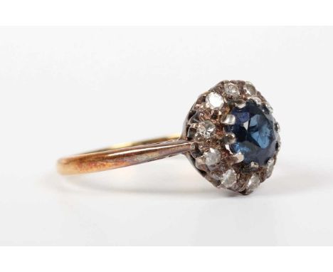 A gold, platinum, sapphire and diamond cluster ring, claw set with the circular cut sapphire within a surround of single cut 