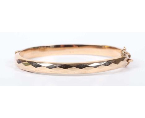 A 9ct gold oval hinged bangle with faceted decoration, Birmingham 1971, weight 10.3g, inside width 6.1cm.