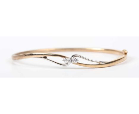 A 9ct two colour gold and diamond oval hinged bangle, the front mounted with three circular cut diamonds in a twist design, w