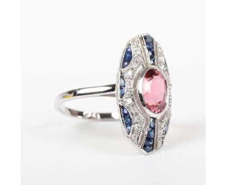 A white gold ring, collet set with an oval cut pink tourmaline at the centre, otherwise mounted with calibre cut sapphires an