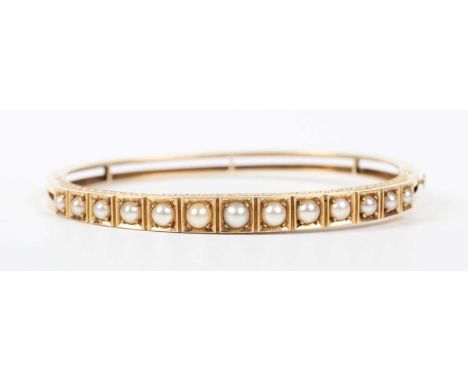 A gold and half-pearl oval hinged bangle, the front mounted with a row of graduated half-pearls each in a square shaped setti