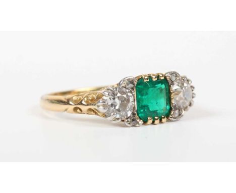 A gold, emerald and diamond ring, claw set with the cut cornered rectangular step cut emerald between two principal circular 