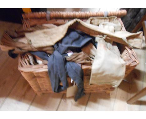 A vintage wicker fishing basket containing a large collection of assorted canvas and other fishing rod bags - various conditi
