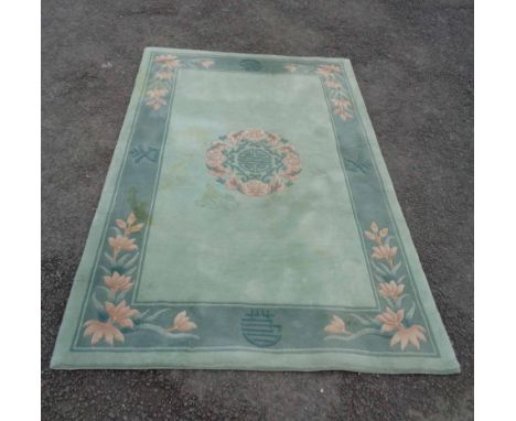 A modern Chinese washed wool rug with central floral medallion and floral sprays on dark green border and light green ground 