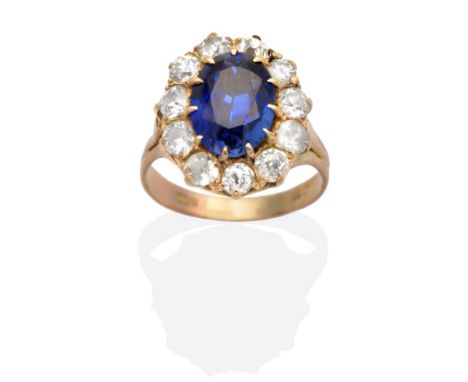 A Sapphire and Diamond Cluster Ring, an oval cut sapphire in a claw setting, within a border of old cut diamonds, to forked s