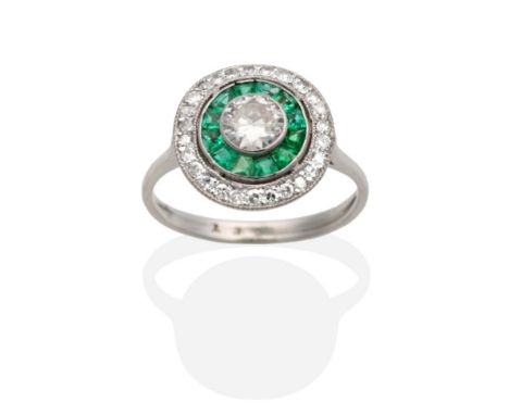 An Art Deco Diamond and Emerald Ring, a central old cut diamond in a rubbed over setting within a circular border or calibré 