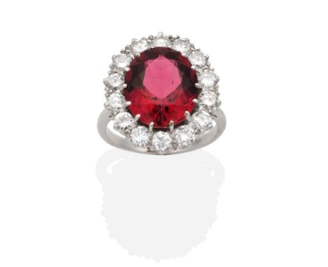 A Pink Tourmaline and Diamond Cluster Ring, an oval cut pink tourmaline in a claw setting, within a border of round brilliant