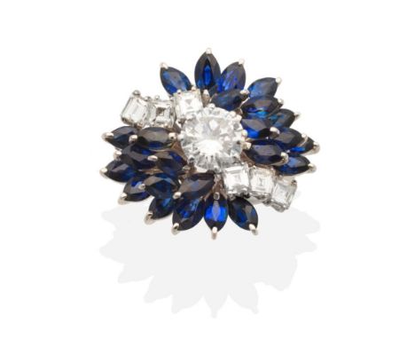 A Diamond and Sapphire Cluster Ring, a central round brilliant cut diamond in a claw setting between a curve of baguette cut 