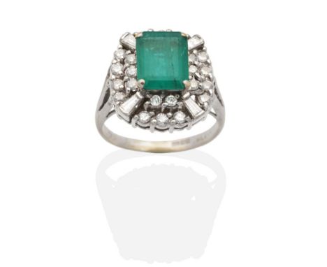 An 18 Carat Gold Emerald and Diamond Cluster Ring, an octagonal cut emerald in a claw setting, within a border of round brill