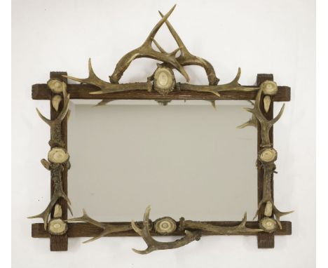 A Black Forest mirror,with a simulated tree trunk frame, mounted with antlers and boar teeth, with a bevelled edge glass plat