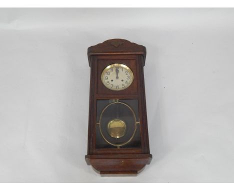 An early 20thC oak cased wall clock, silvered dial bearing Arabic numerals, eight day movement with coil strike, case with gl