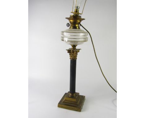 A corinthian column oil lamp, with brass and black lacquer base, clear glass reservoir and converted to electricity