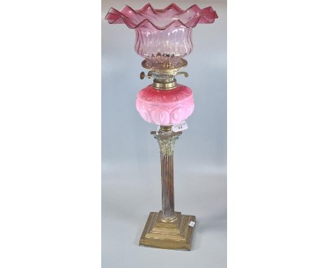 Early 20th century double oil burner lamp, having frilled cranberry glass shade above a pink ceramic moulded reservoir on Cor