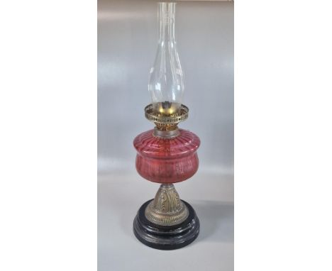 Early 20th century double oil burner lamp having cranberry glass reservoir above a brass and ebonised wooden base. (B.P. 21% 