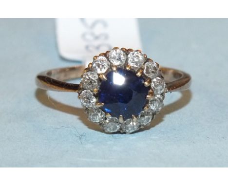 A sapphire and diamond cluster ring, the round cut sapphire claw set within a border of twelve old brilliant cut diamond in u