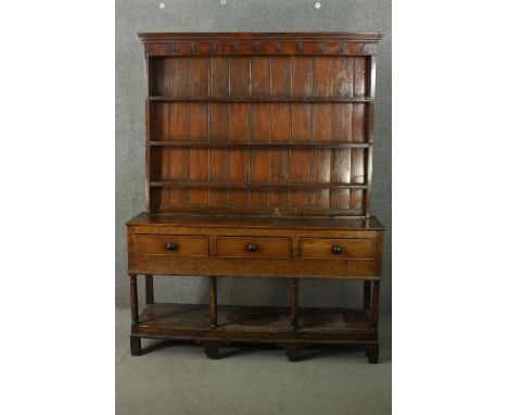 An 18th century oak dresser, the plate rack with three shelves, over three short drawers, on ionic column supports, joined by