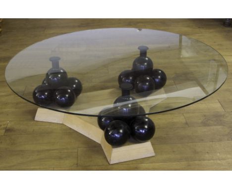 A MODERN GLASS TOP CANNONBALL TABLE, the circular glass top raised on three columns of five cannonballs and wooden plinth, H 