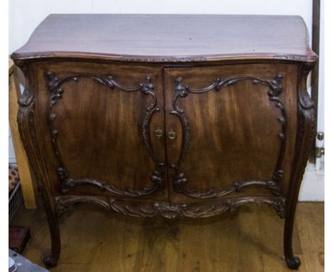 A CHIPPENDALE STYLE MAHOGANY COMMODE, of bombe form, the shaped top with carved detail to the edges over a pair of shaped doo