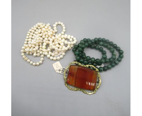 Ornate yellow metal rectangular brooch set with large agate, a string of jade beads with white metal clasp, a double knotted 
