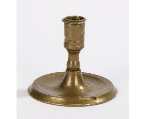 16th Century French brass candlestick, the shortened candle socket on a tapering stem leading down to broad circular feet, 7.