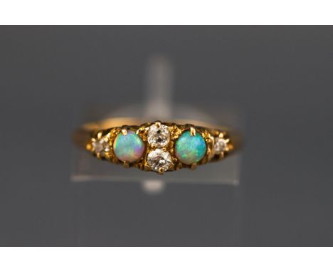 An early 20th century gold, opal and diamond ring, centered with two small old-cut diamonds, flanked by cabochon white opals 