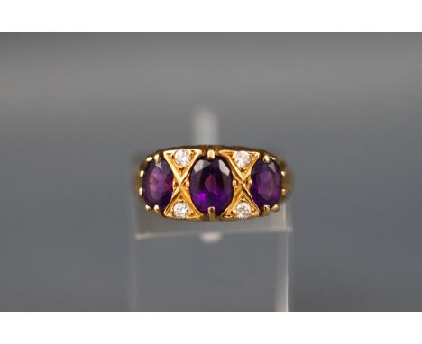 An 18ct gold, amethyst and diamond dress ring, the three graduated oval mixed-cut amethysts spaced by pairs of small round br