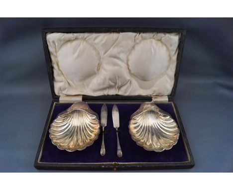 A pair of silver shell-shaped butter dishes each on three ball feet, with two small butter knives, Sheffield 1925 by Harrison