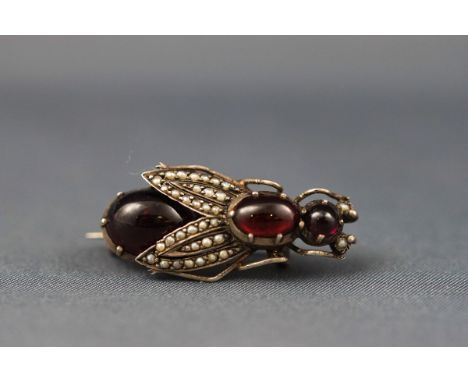 A Continental white metal, garnet cabochon and seed pearl brooch in the form of a winged insect, approx. 32mm long overall.