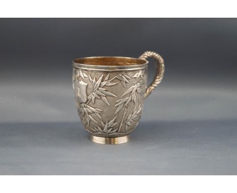 A Chinese export silver small mug with a scroll handle and profusely embossed with bamboo on a matt ground and with a shield 