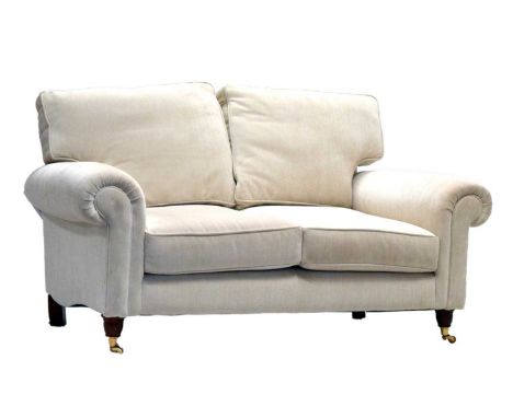 Laura Ashley (attr.) cream upholstered two-seater sofa, the turned front legs with brass caps and castors, 161cm x 92cm x 82c