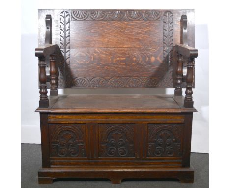 An oak monk’s bench, early 20th Century, rectangular top with carved lunette frieze, turned supports, box base with carved pa