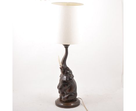 A carved hardwood table lamp, in the form of a elephant, sitting and balancing a ball on the end of its trunk, 43cm.