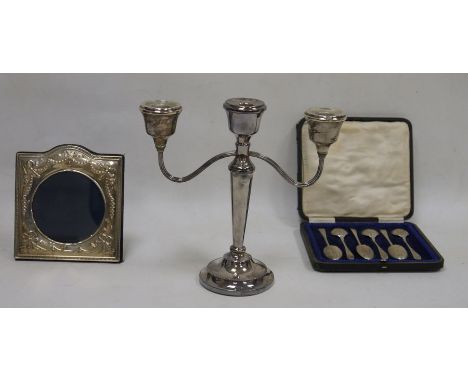 A silver picture frame, a cased set of six spoons and a three light candelabrum, the frame with arched top cast with ribbon t