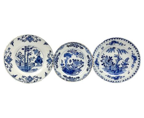 Three English Delftware plates, each decorated with a Chinese inspired scene with peonies, fir trees, and fence, smallest exa