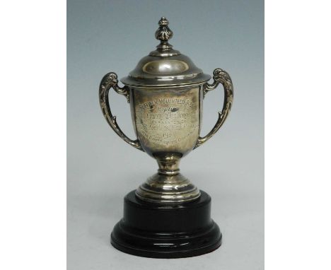 A George V silver trophy cup and cover, the domed cover with embossed finial, the body with leaf capped twin handles raised o