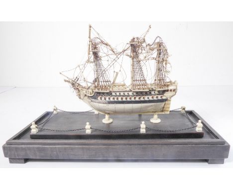 A modern copy of a Napoleonic prisoner of war style bone model of a man o' war with two cannon decks, upon rectangular staine