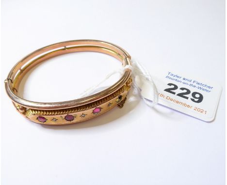 A 19th century gem-set yellow gold hinged bangle; the top section set with four red stones (one unmounted) separated by a dia