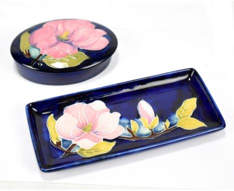 MOORCROFT; a tubeline decorated 'Magnolia' pattern lidded oval dish, width 13cm, and rectangular dish both on navy grounds, b