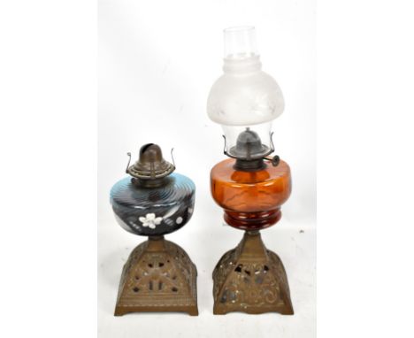 Two Victorian oil lamps on pierced bases, the taller with orange glass reservoir beneath chimney featuring opaque shade, heig