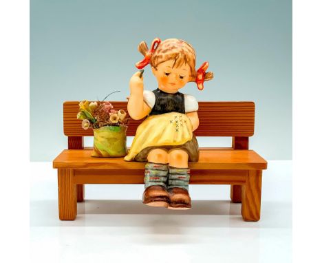 A figure of a young girl in dress and yellow apron with pigtails that is made to be seated on her wooden bench along with a p