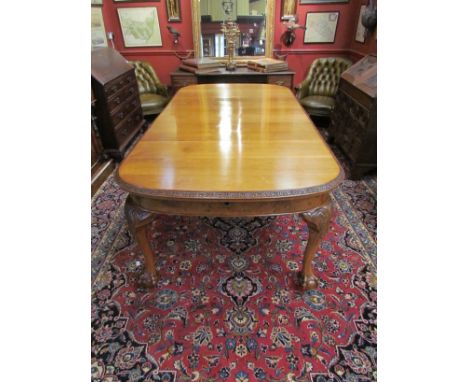 A figured walnut extending dining table with two extra leaves and winding handle the carved leaf edged top over claw and ball