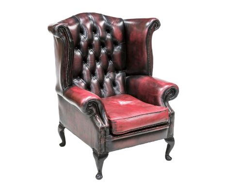 A GEORGIAN STYLE RED LEATHER BUTTON BACK WING CHAIR, raised on short cabriole legs 