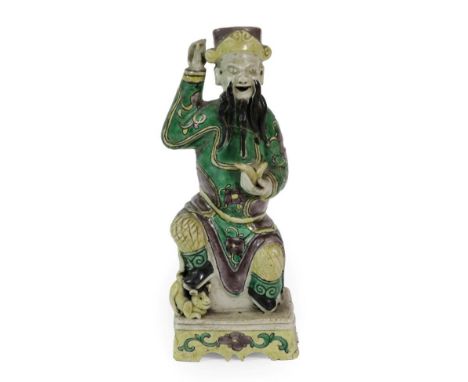 A Chinese Bisque Porcelain Figure of an Immortal, Kangxi, the seated figure wearing a cylindrical hat holding a fruit, his ri